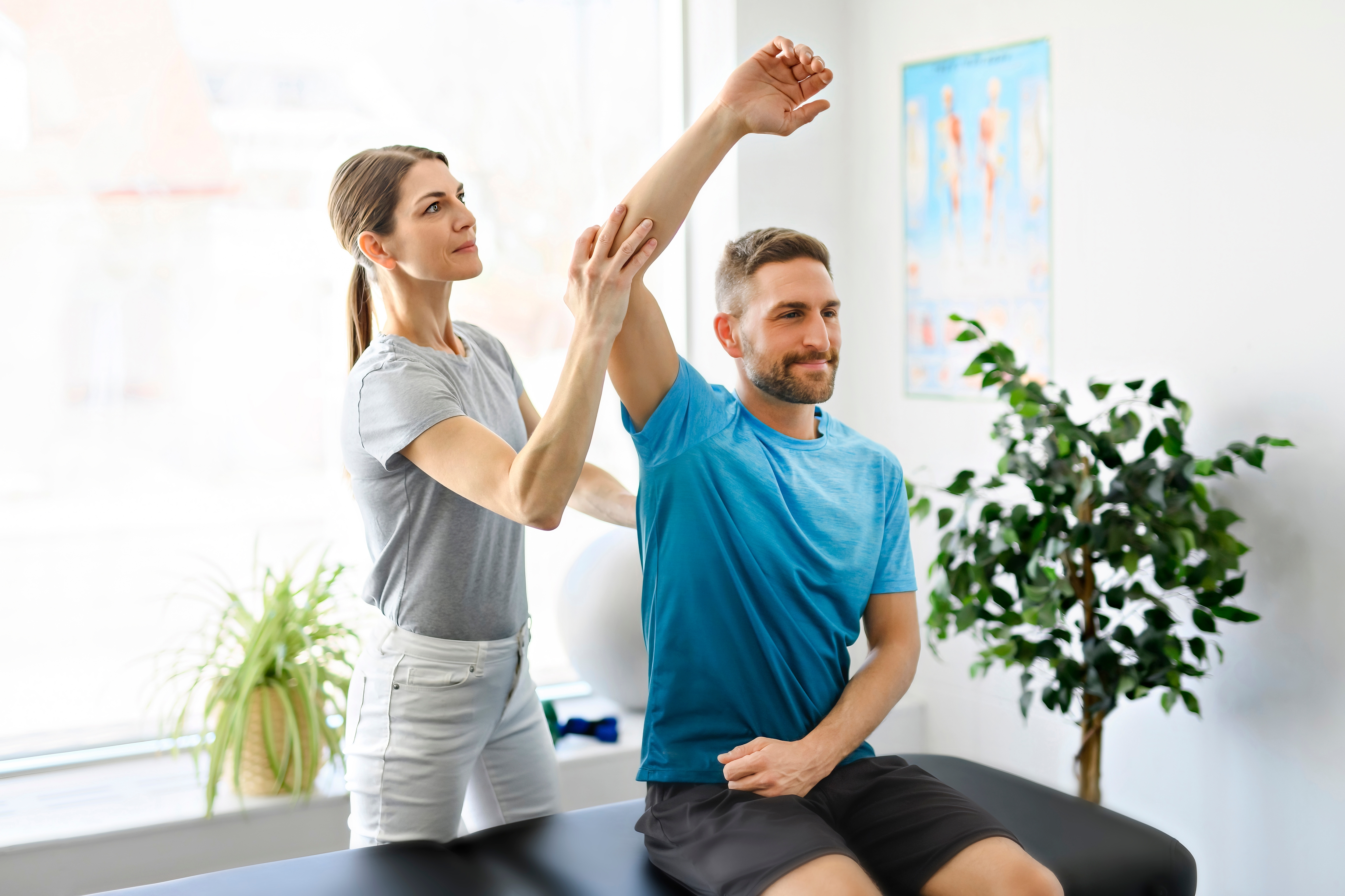 Woman therapist stretching male patient's arm during assisted stretching session