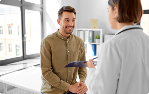A smiling male patient consulting with a female doctor holding a clipboard.
