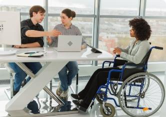 An employee using a wheelchair collaborating with colleagues in a bright office meeting.